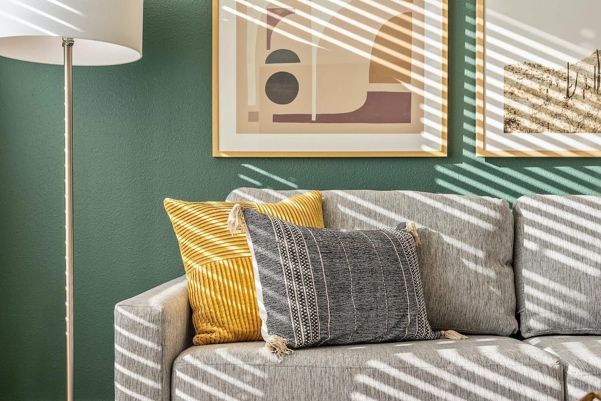 Sala de estar com sofá, duas almofadas, abajur e duas obras de arte emolduradas na parede.