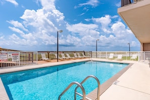 A swimming pool with a metal ladder, surrounded by lounge chairs and a fenced deck area. - Ocean Breeze East 702- 2BR/ 2BA (Perdido Key)