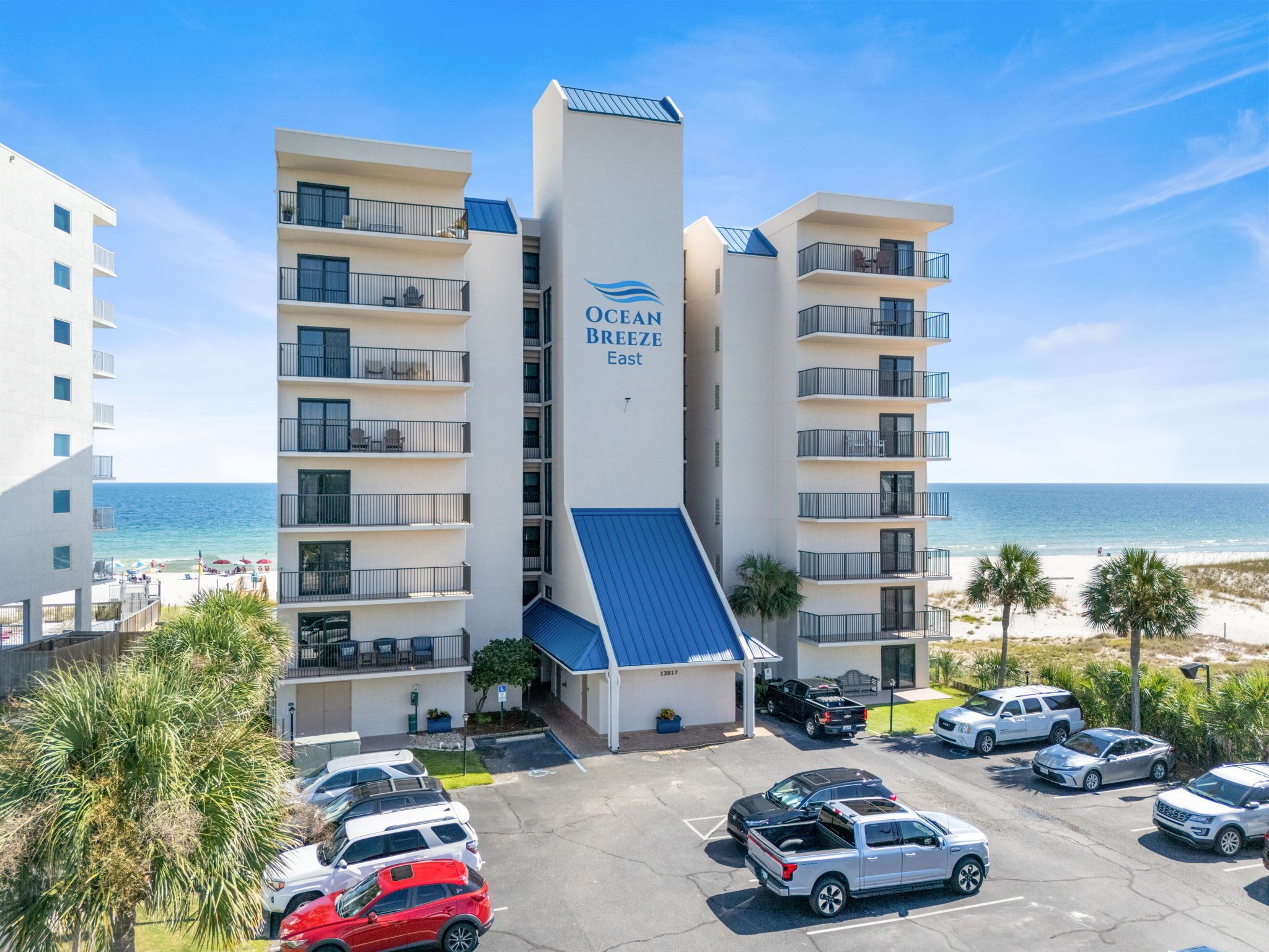 A multi-story hotel with balconies, a parking lot, and a view of the beach.