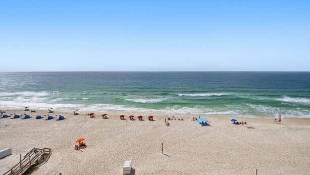 Una spiaggia con file di ombrelloni e lettini, una torretta per i bagnini e una passerella di legno che conduce all'acqua.