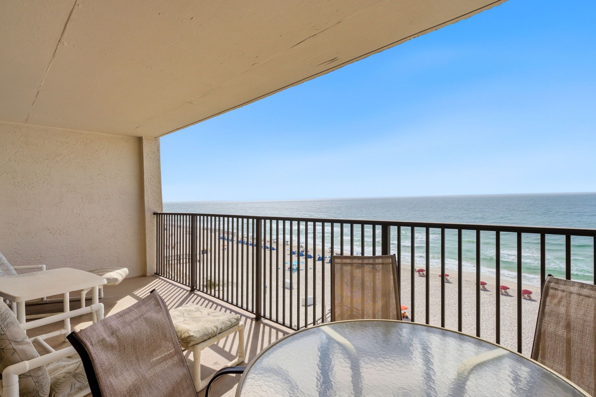 A balcony with a view of the beach, a table, and chairs.