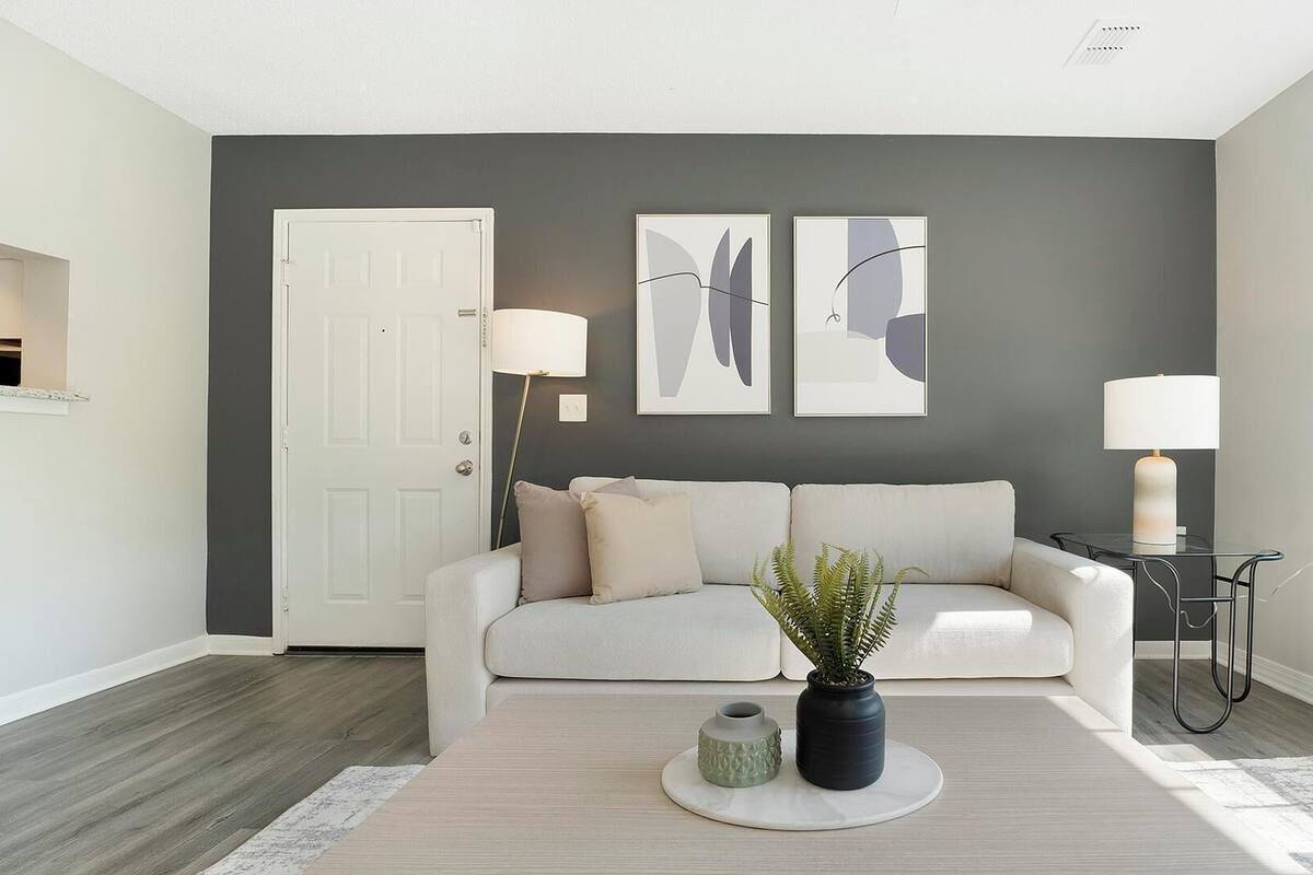 Un salon moderne avec un mur d’accent gris, un canapé blanc, une table basse ronde agrémentée d’une plante et deux lampadaires.