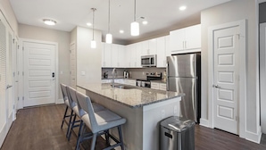 A modern kitchen with white cabinets, stainless steel appliances, and a granite countertop. - Landing Furnished Apartments near YSM (New Haven)