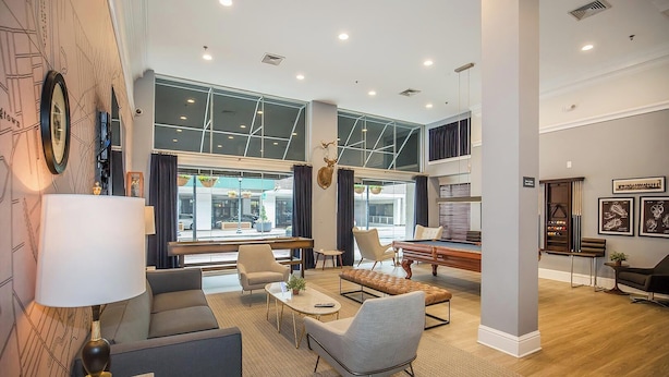 A modern living room with a pool table, comfortable seating, and large windows. - Landing Furnished Apartments near YSM (New Haven)