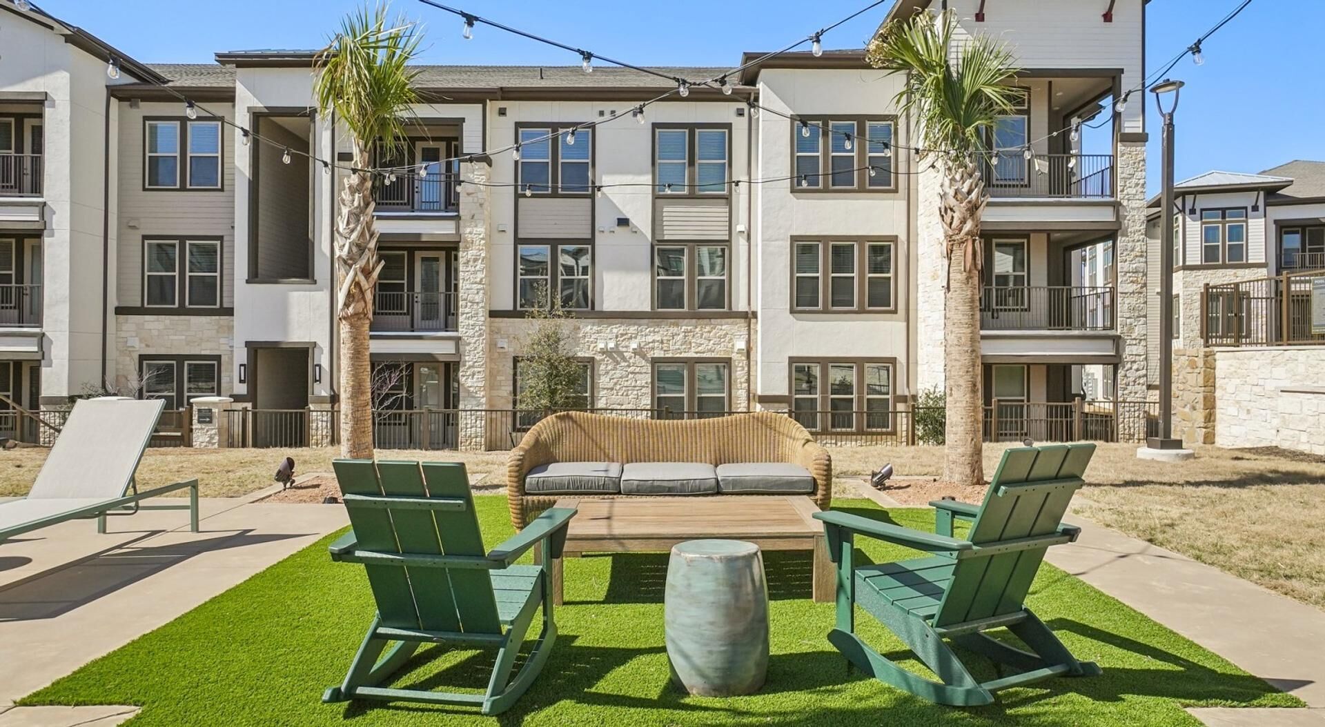 Un immeuble résidentiel à plusieurs étages doté de balcons, d’un patio avec des chaises vertes et d’un espace de détente central.