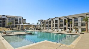 A swimming pool with lounge chairs and a building with multiple floors and balconies. - Landing Apartments - Melissa, TX (Melissa)