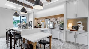 Cocina moderna con una isla central, taburetes de bar, iluminación colgante y un salpicadero de mármol.