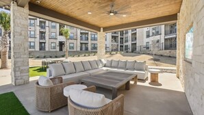 A covered outdoor seating area with a sectional sofa, wicker chairs, and a coffee table. - Landing Apartments - Melissa, TX (Melissa)