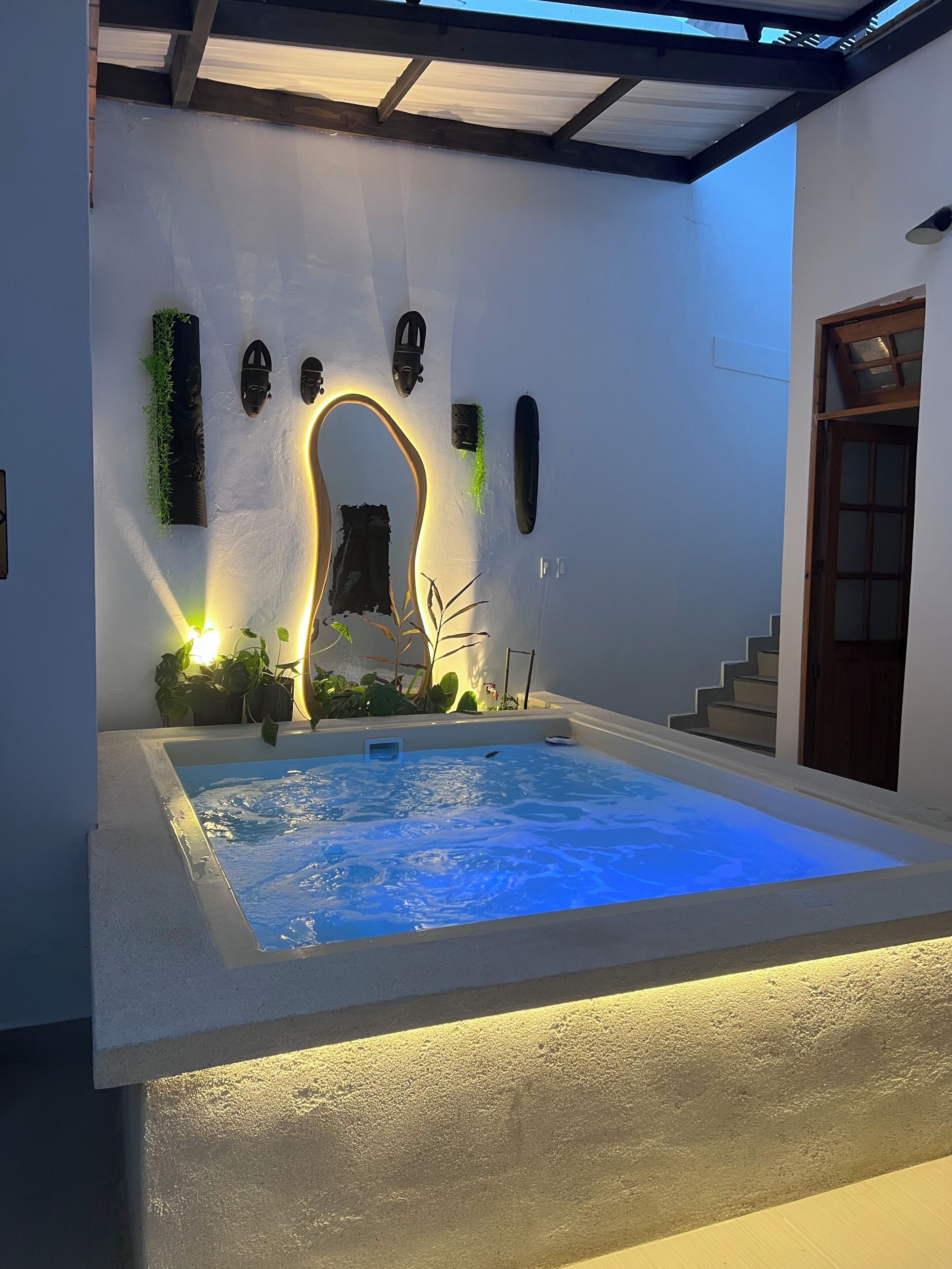 Una piscina interior moderna con un diseño de arco distintivo, rodeada de plantas y una escalera.