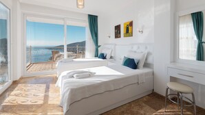A hotel room with two beds, a desk, a chair, a balcony with a view of the sea, and a large window. - Stunning Sea View Villa in Kalkan with Private Pool, 4 Bedrooms, 8 Guests (Antalya)