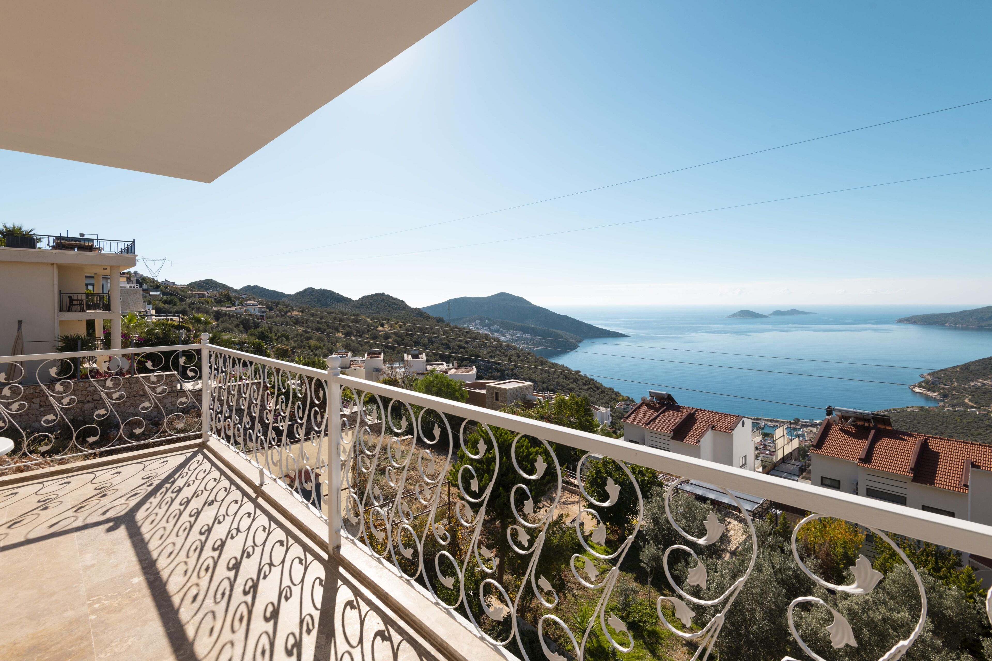 A balcony with ornate metal railings overlooking a coastal landscape with mountains and a body of water.