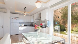 A modern kitchen with white cabinets, a stainless steel refrigerator, and a dining area with a glass table and bench. - Stunning Sea View Villa in Kalkan with Private Pool, 4 Bedrooms, 8 Guests (Antalya)