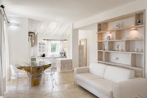 Una sala moderna con una mesa de comedor de vidrio, sofá blanco y estanterías de madera con objetos decorativos.
