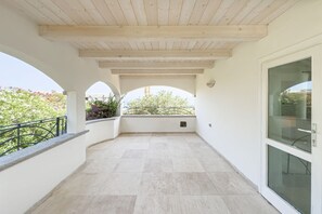 Ein überdachter Balkon mit Fliesenboden, weißen Wänden und Holzboden.