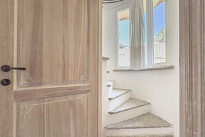 Una puerta de madera con cerradura, que da a una escalera de piedra y un ventanal con cortinas.