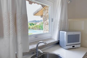 A kitchen with a built-in microwave, a window with a view of greenery and mountains, and a stone wall. - <i>Suspended between Gallura granite and the blue of the sea, just minutes from Porto Cervo, where luxury is enjoyed in private.</i>In the prestigious setting of the <b>Costa Smeralda</b>, in <b>Abbiadori</b> and just <b>4 km from Porto Cervo</b>, Villa  (Abbiadori)