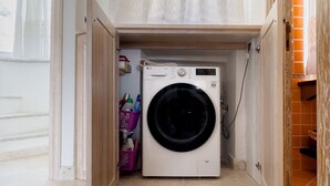 Pieni ja käytännöllinen pyykinhuoltotila, jossa on pyykinpesukone, pieni hylly pyykinpesutarvikkeille ja ovi, joka johtaa toiseen huoneeseen.