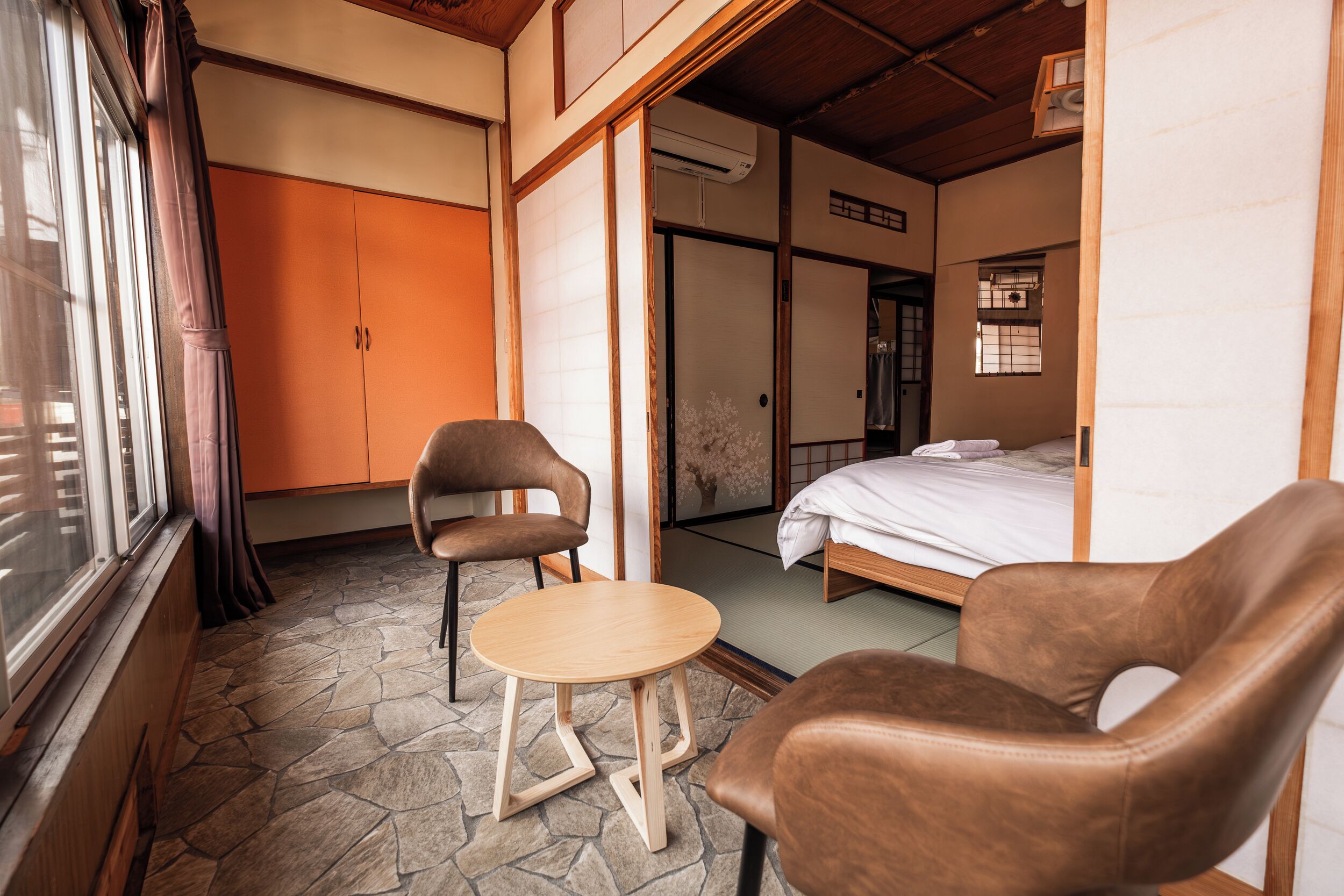 A room with a bed, two chairs, a small table, and a window with curtains.