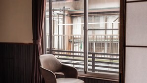 Una habitación con cama, una silla, una mesita y un ventanal con vistas a edificios.