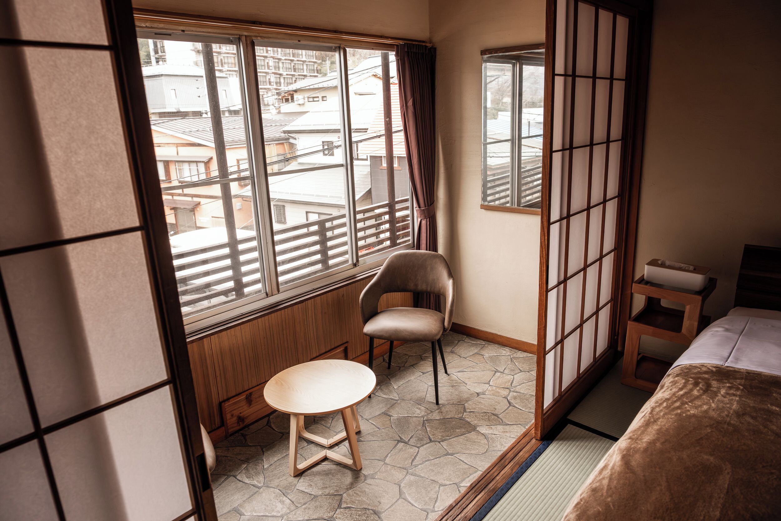 Une chambre d’hôtel avec vue sur les immeubles, une chaise, une petite table et un lit.