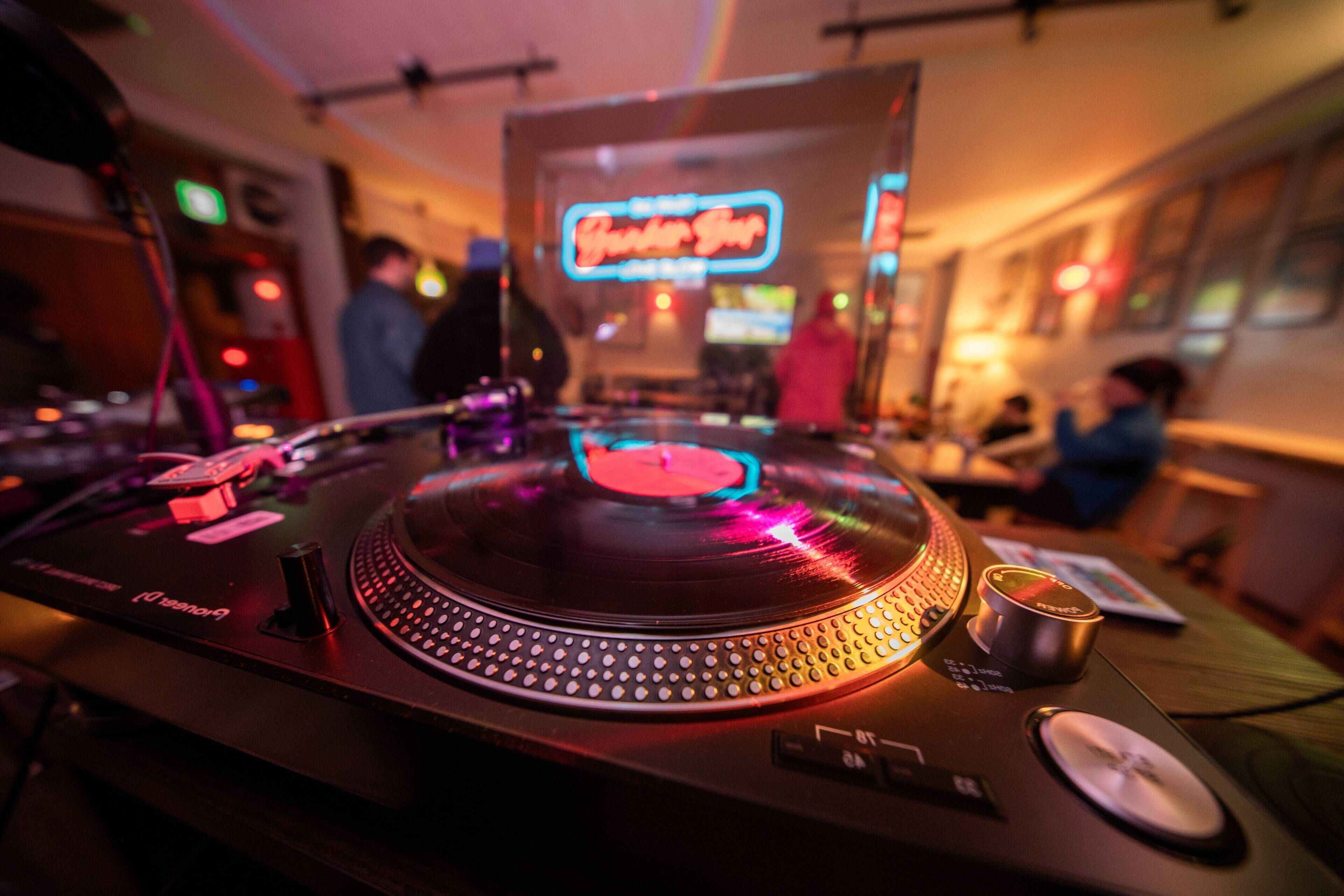 A DJ booth with a neon sign, control knobs, and a record player.