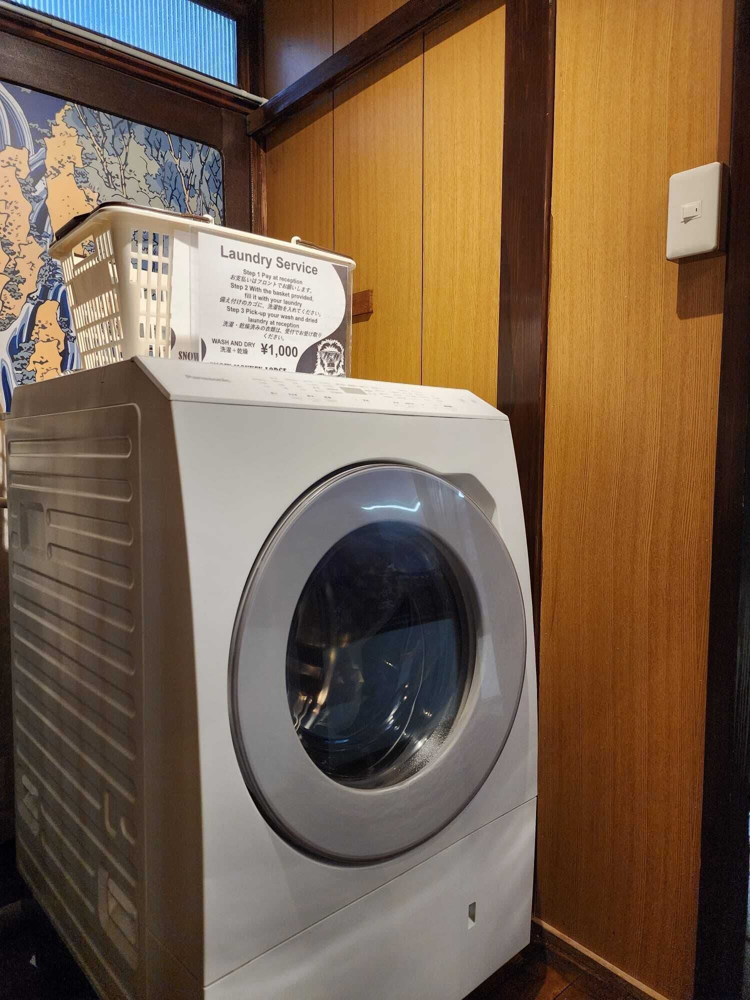 Una lavadora de carga frontal, un letrero de servicio de lavandería, una cesta y una pared de madera.