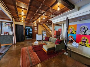 A hotel lobby with a wooden ceiling, a sofa, a coffee table, a rug, and a wall with colorful monkey artwork. - Snow Monkey Lodge - Hostel  (Yamanouchi)