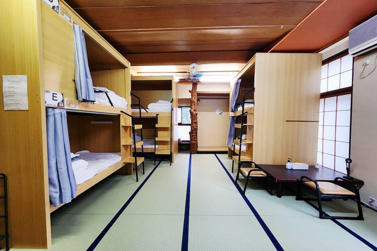 A dormitory room with bunk beds, tatami mats, a small table, and a chair.
