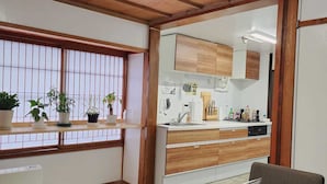 Una habitación con techo de madera, una mesa de comedor con sillas, una zona de cocina con armarios y una ventana con plantas en macetas.