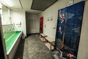 A bathroom with a green-tiled sink, a bench, and a blue curtain with koi fish design.