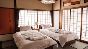 Una habitación al estilo japonés tradicional con suelo de tatami, dos camas con ropa blanca, techo de madera y amplios paneles de shoji.