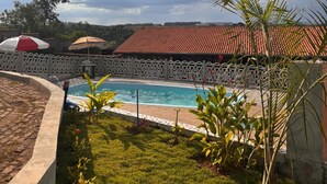 A swimming pool with a tiled roof, surrounded by a white fence, and a grassy area with plants and umbrellas. - Cozy country house surrounded by nature, with a beautiful sunset view. (Piracicaba)