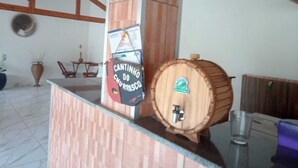 A wooden counter with a sign, a wooden barrel, and a glass on a table. - Cozy country house surrounded by nature, with a beautiful sunset view. (Piracicaba)