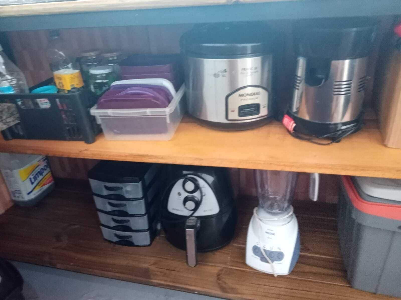 Ein Küchenregal mit einer Plastikbox, einer Mondial Kaffeemaschine, einem Mixer und einer Kaffeemühle.