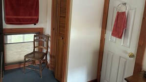 A room with a wooden door, a window with blinds, a wooden chair, and a red towel hanging on the wall. - Charming 1-bedroom apartment in Worcester, private swimming hole. (Worcester)