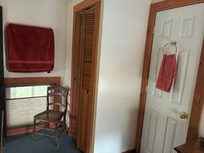 A room with a wooden door, a window with blinds, a wooden chair, and a red towel hanging on the wall. - Charming 1-bedroom apartment in Worcester, private swimming hole. (Worcester)