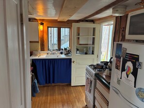 A kitchen with wooden floors, a stove, a refrigerator, and a window with a view of the outside. - Charming 1-bedroom apartment in Worcester, private swimming hole. (Worcester)