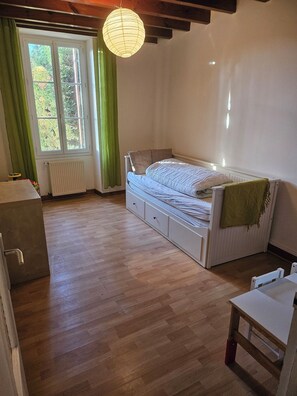A bedroom with a bed, a radiator, a window with curtains, a wooden floor, and a hanging light fixture. - Charentais country house surrounded by vineyards with heated swimming pool (Mosnac)