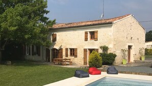 A stone building with a swimming pool, a patio with seating, and a large tree. - Charentais country house surrounded by vineyards with heated swimming pool (Mosnac)