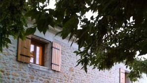A stone building with wooden shutters, a table with a red tablecloth, and a grill outside. - Charentais country house surrounded by vineyards with heated swimming pool (Mosnac)