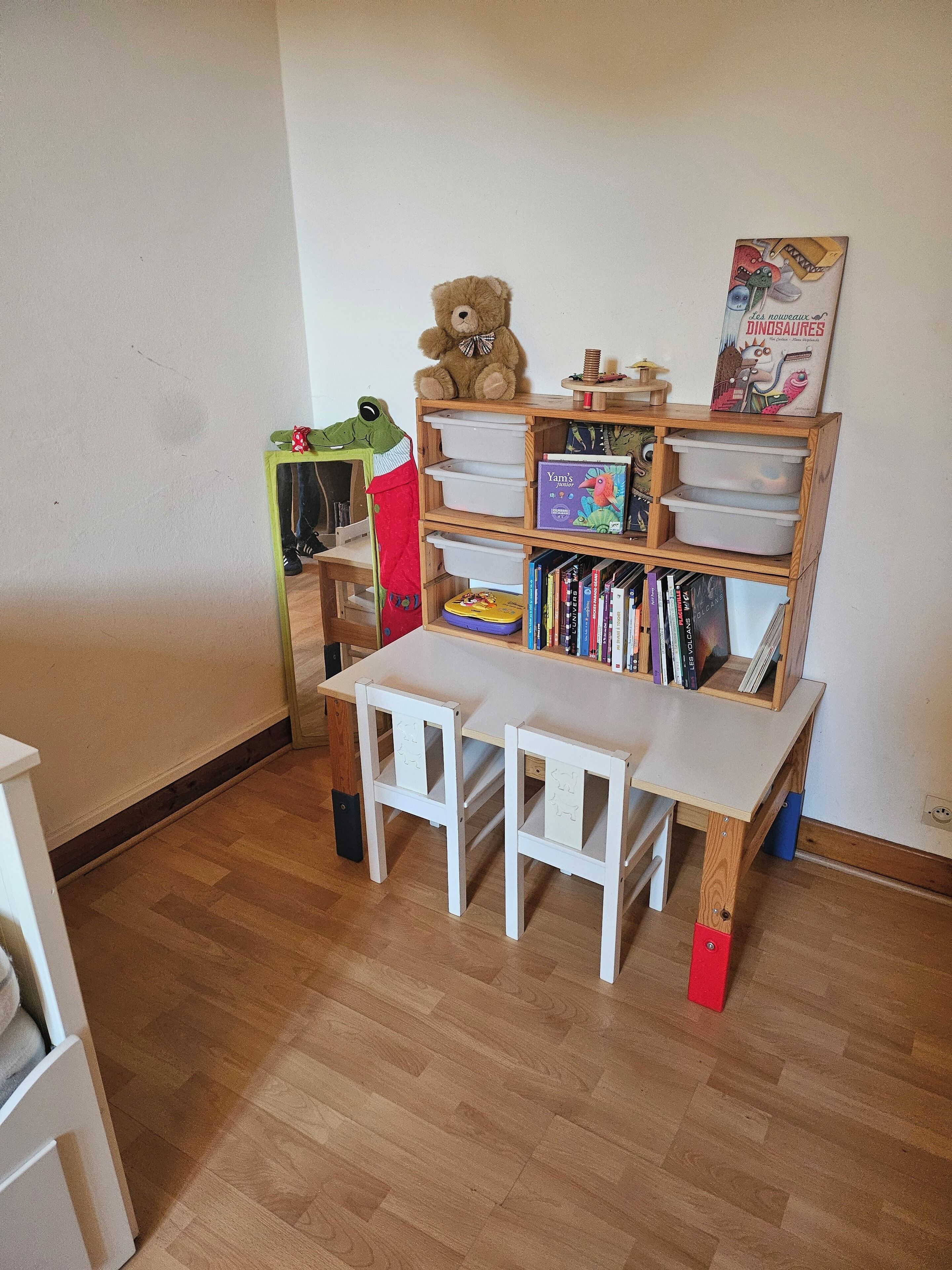 A room with a wooden bookshelf, a small table with chairs, and a mirror.