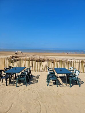 A beachside seating area with tables and chairs, a bamboo fence, and a view of the ocean. - Charentais country house surrounded by vineyards with heated swimming pool (Mosnac)