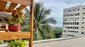 En balkon med krukker med planter, udsigt til en bygning og en palme.