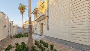 A residential building with a gated entrance, a palm tree, and a pathway with plants. - Alsawah|Luxury 6BR Villa with Private Pool (Sheikh Zayed City)