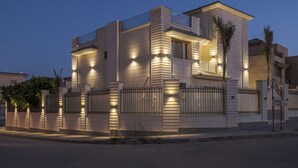 A modern two-story house with a balcony, a gated entrance, and a well-lit facade. - Alsawah|Luxury 6BR Villa with Private Pool (Sheikh Zayed City)