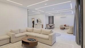 A modern living room with a sectional sofa, a coffee table, and a dining area in the background. - Alsawah|Luxury 6BR Villa with Private Pool (Sheikh Zayed City)