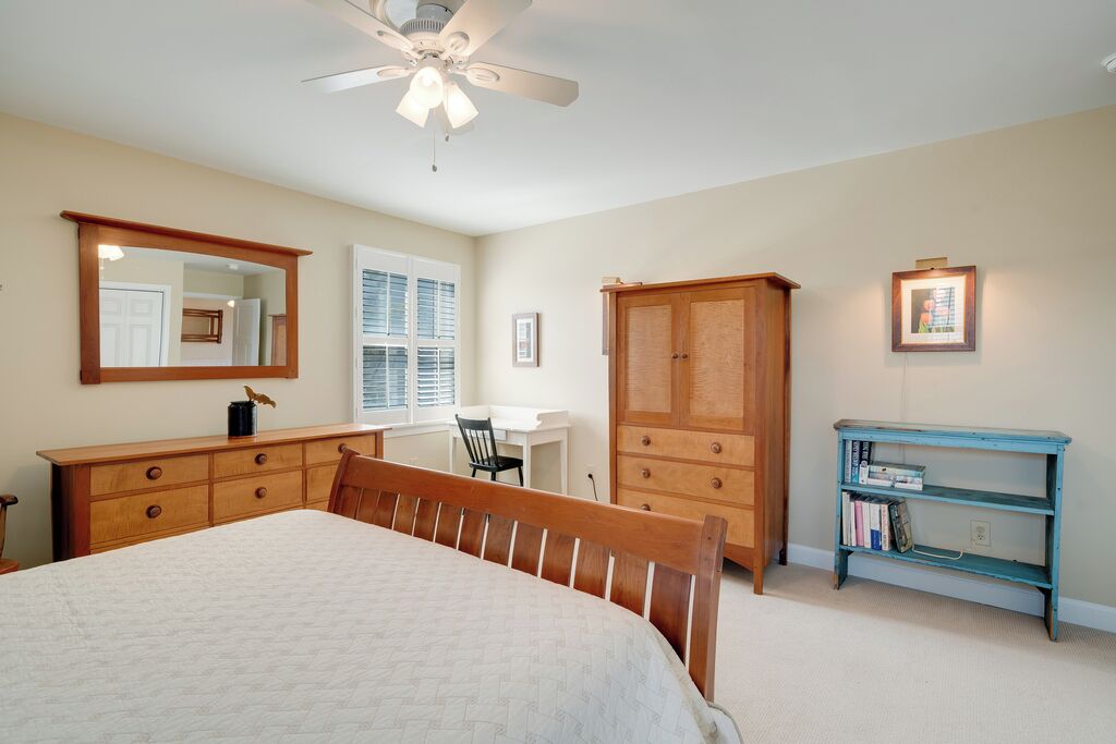 Une chambre à coucher comprenant un lit, un bureau, une armoire, une chaise, une bibliothèque et un ventilateur de plafond.