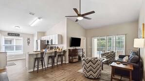 A modern kitchen with a dining area, a living room with a sofa and ottoman, and a ceiling fan. - New Single-Level Private Pool Home with Game Room | Gated Community | 2 Master Bedrooms | Sleeps 10 (Davenport)