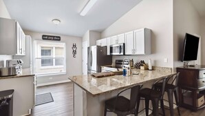 A modern kitchen with white cabinets, a granite countertop, a built-in microwave, and a large island with bar stools. - New Single-Level Private Pool Home with Game Room | Gated Community | 2 Master Bedrooms | Sleeps 10 (Davenport)