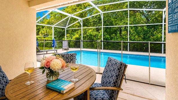 A pool area with a glass enclosure, a table with a book and glasses, and a chair. - New Single-Level Private Pool Home with Game Room | Gated Community | 2 Master Bedrooms | Sleeps 10 (Davenport)